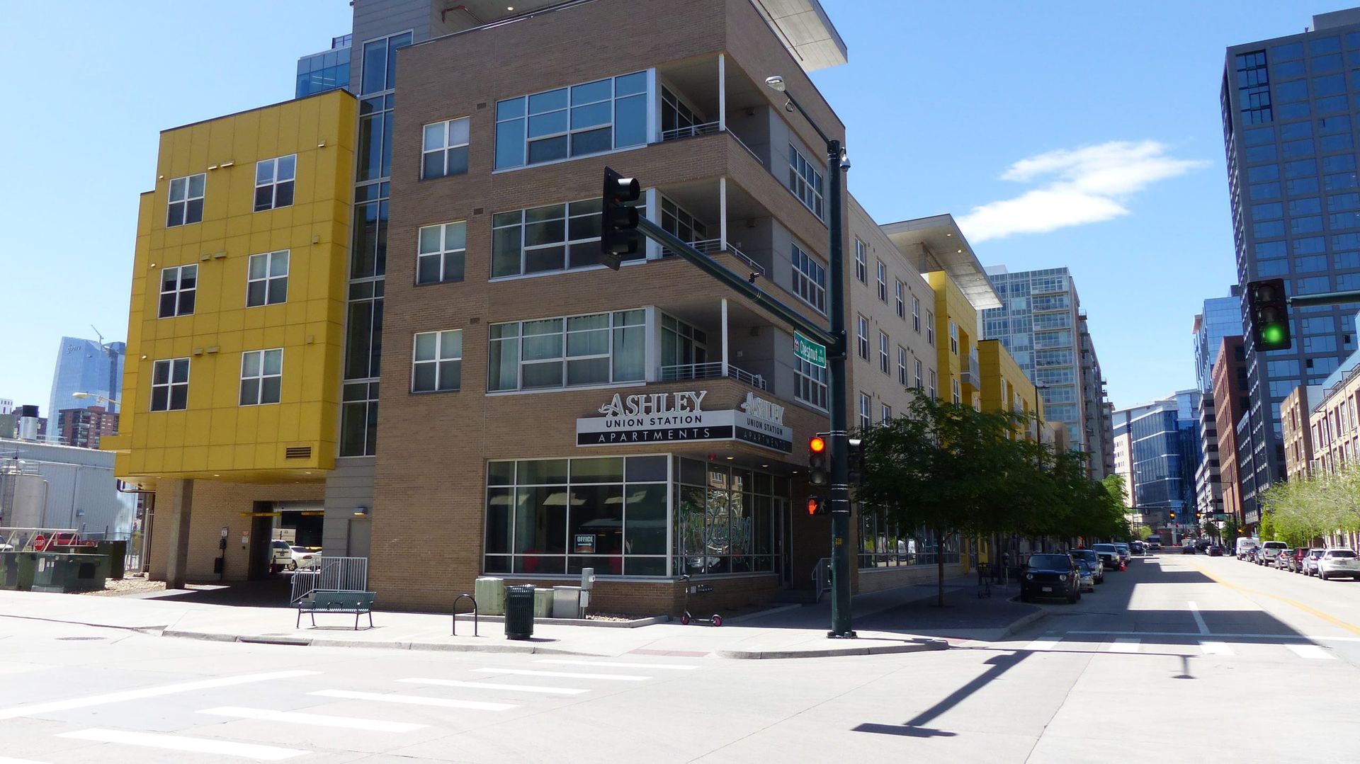 A multi-story corner apartment building with yellow and brown brick facades, located on a city street under a blue sky.
