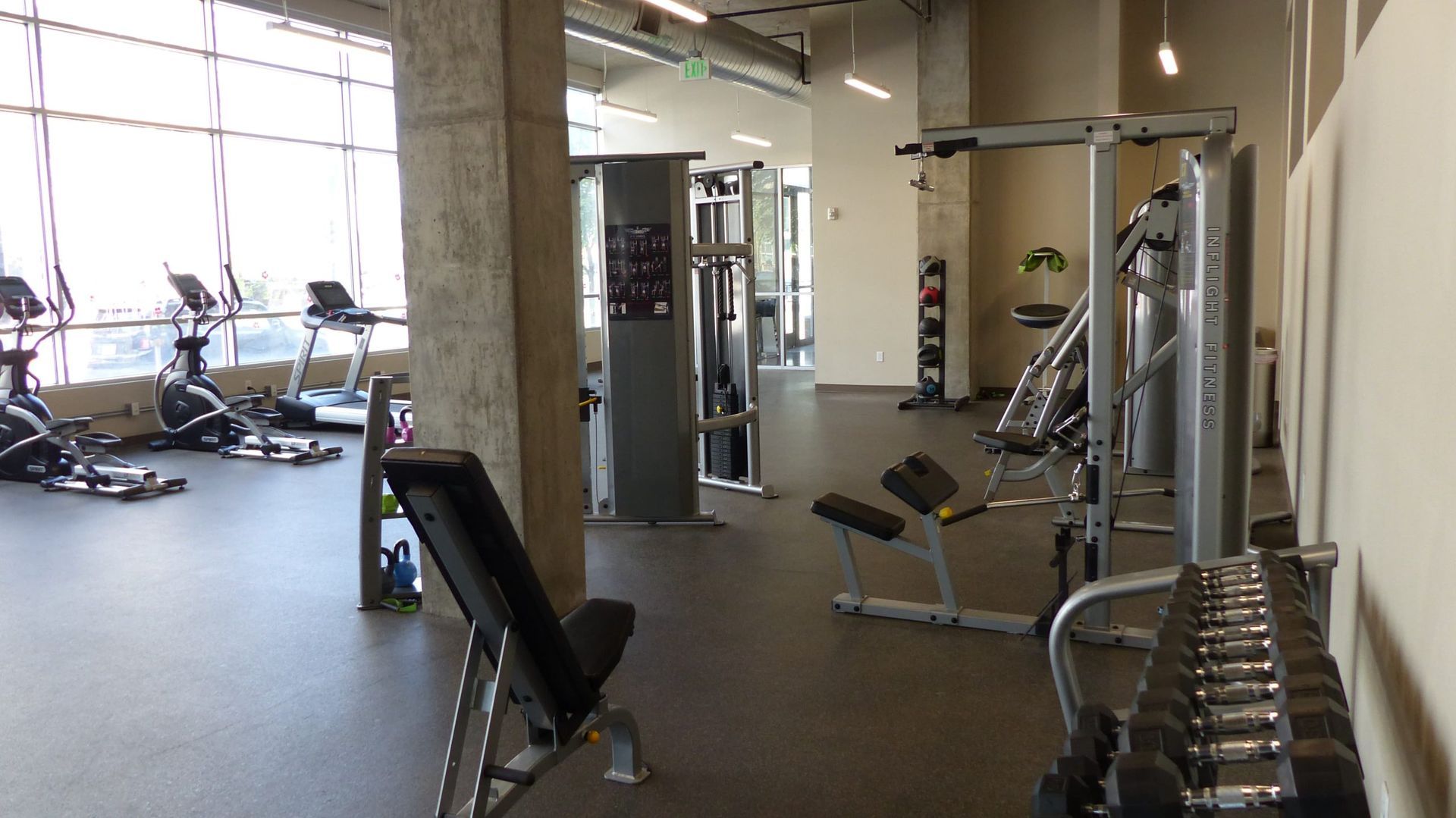 An indoor gym with workout equipment, including treadmills, weight machines, and a rack of dumbbells.