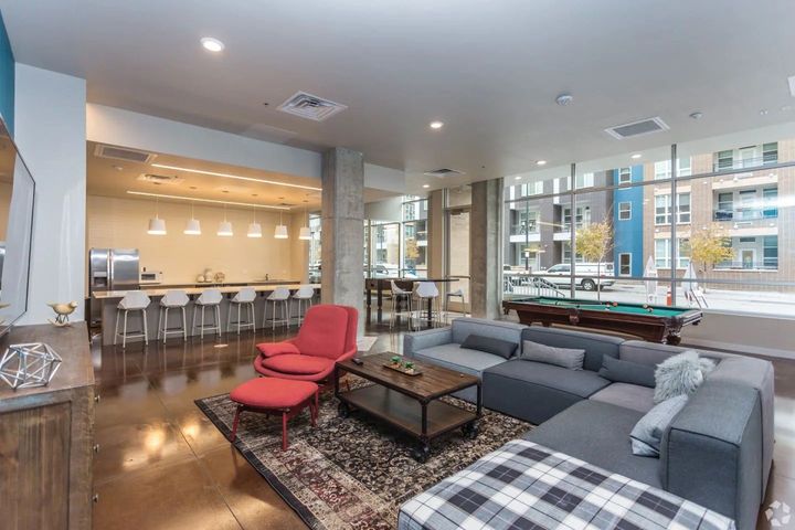 A modern lounge area with a grey sectional, red armchair, coffee table, kitchen counter with stools, and pool table.