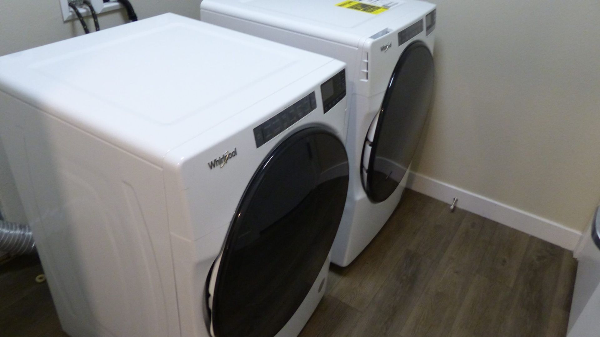 Two white Whirlpool washing machines with dark circular doors side-by-side in a room with wood flooring.
