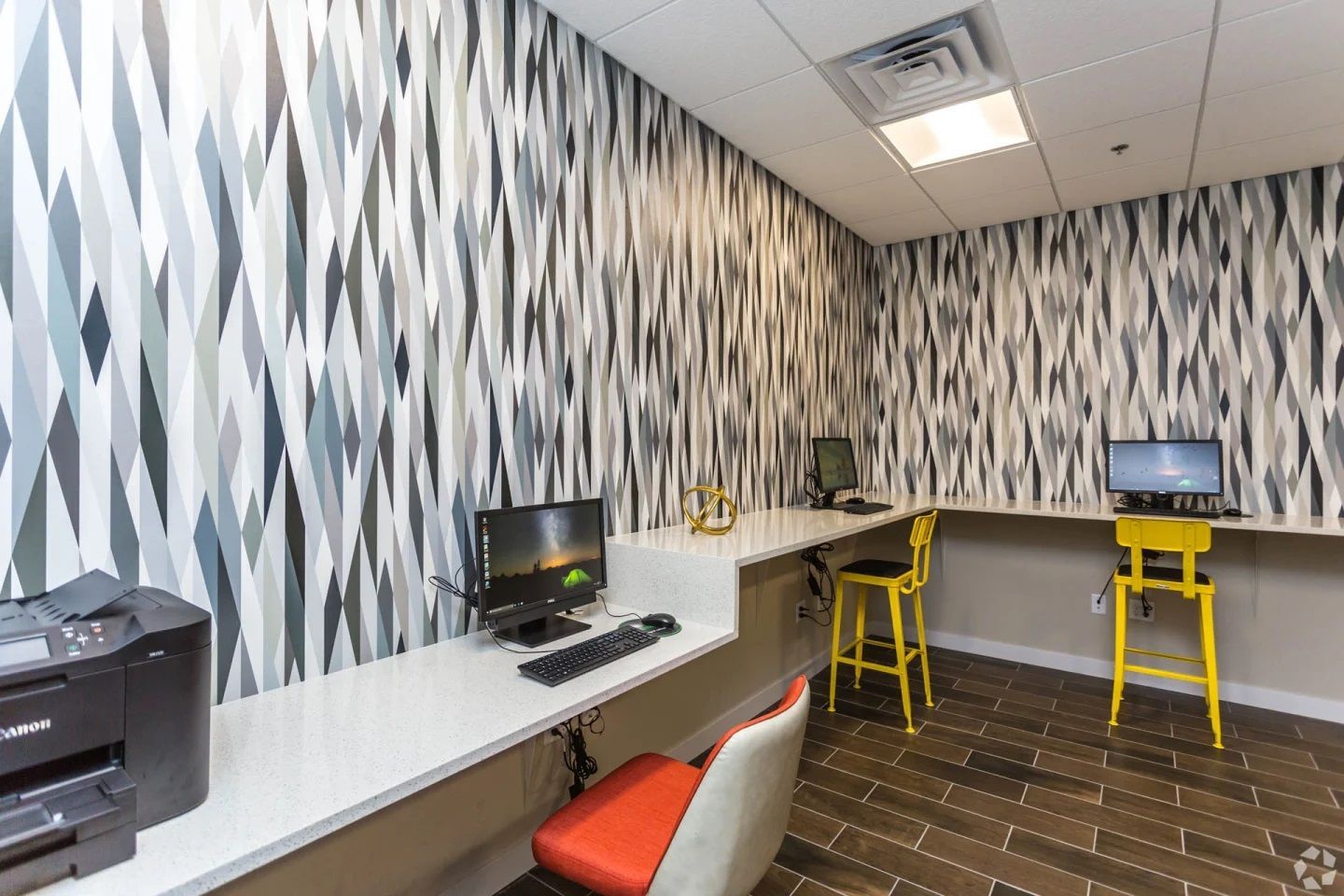 A business center with two computer workstations, yellow chairs, and patterned wallpaper.