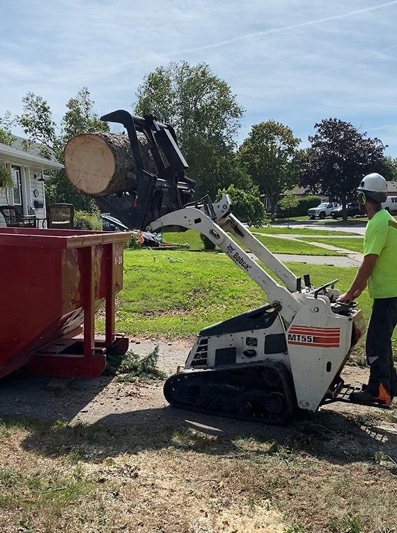 A man is standing next to a small bulldozer carrying a log.