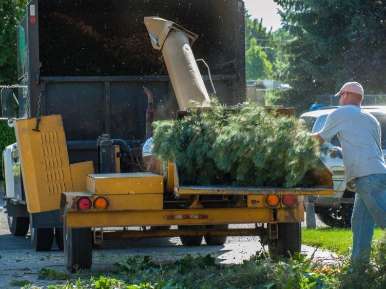 A man is loading a tree chipper into a truck.