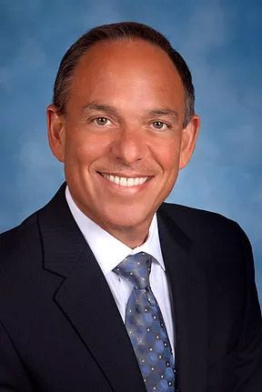 A smiling doctor in a lab coat with a stethoscope around his neck.
