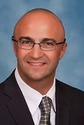 A smiling doctor in a lab coat with a stethoscope around his neck.