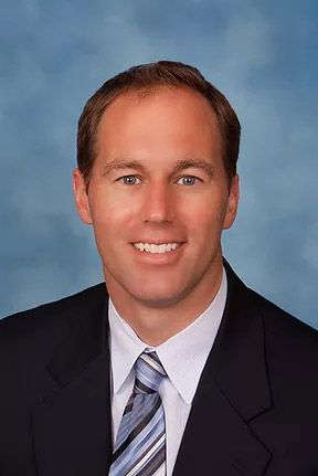 A smiling doctor in a lab coat with a stethoscope around his neck.