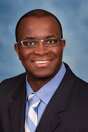 A smiling doctor in a lab coat with a stethoscope around his neck.