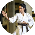 A woman in a white karate uniform with a black belt is standing in a circle.