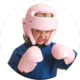 A young boy wearing a pink helmet and pink boxing gloves.