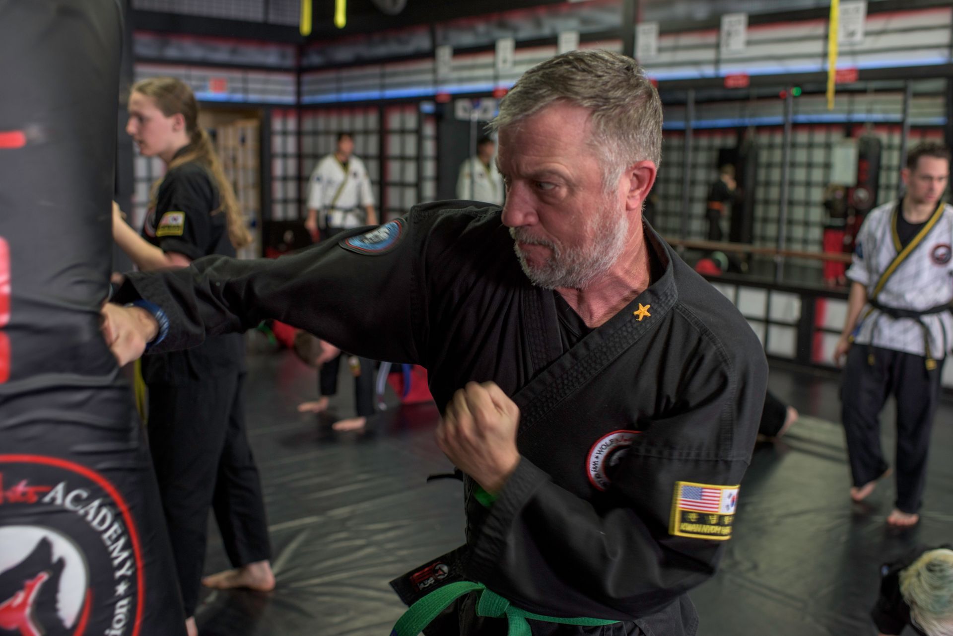 A man is practicing martial arts with a group of people in a gym.