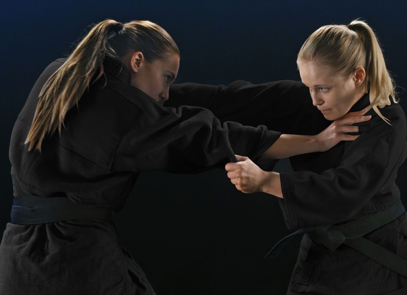 Two women in black kimonos are practicing martial arts