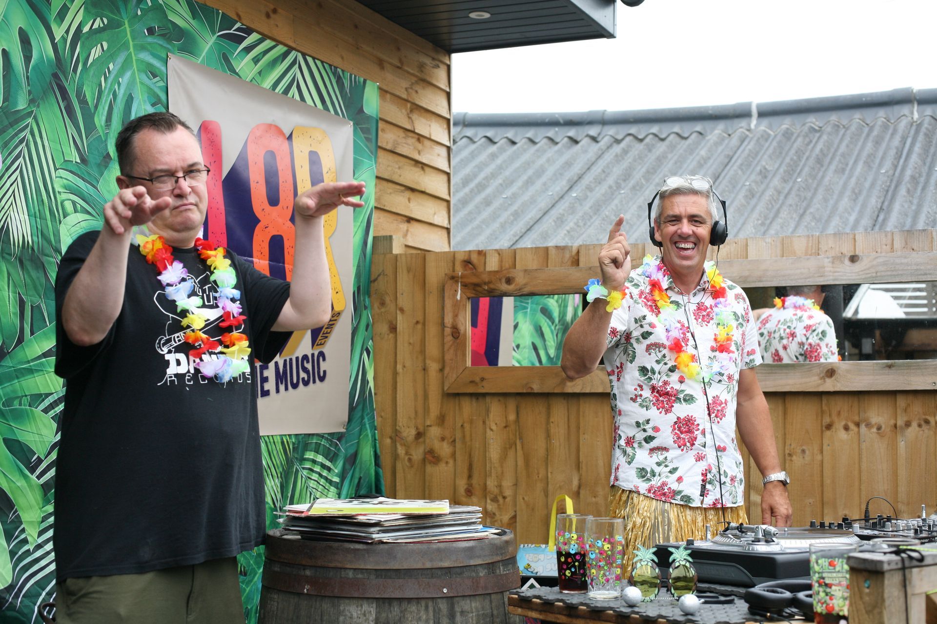 Two men wearing hawaiian shirts and headphones are standing next to each other.