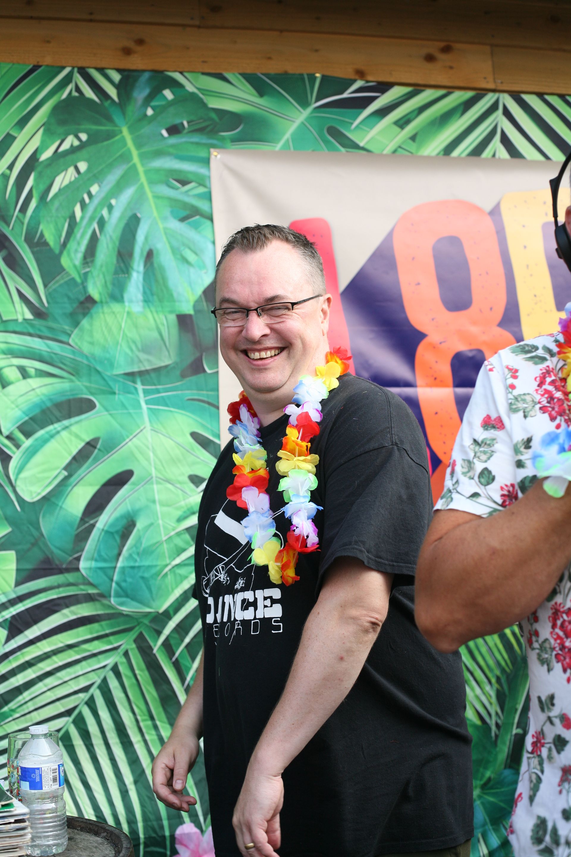 A man wearing a lei is smiling in front of a tropical background.