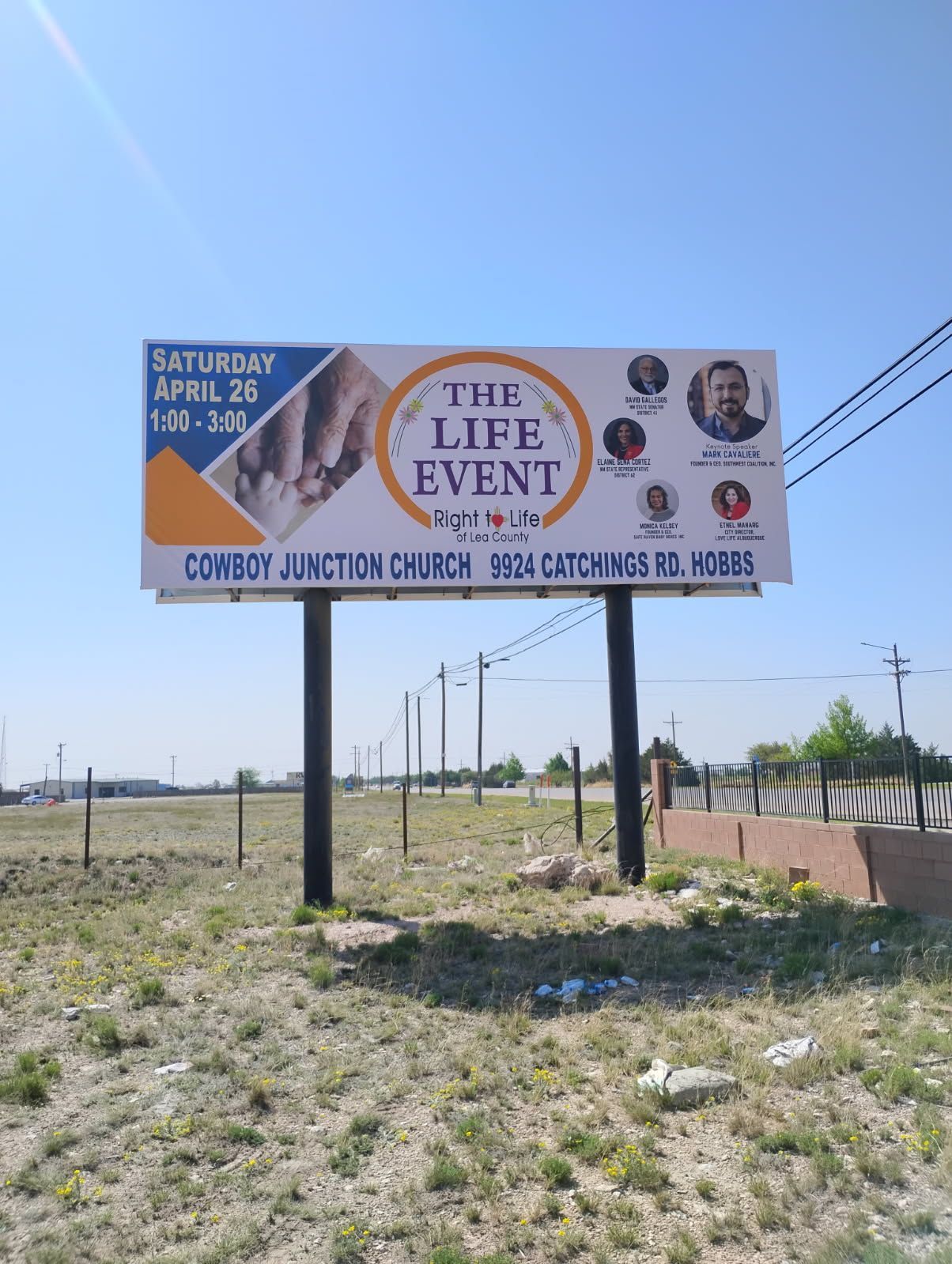 A billboard for the life event is sitting in the middle of a grassy field.