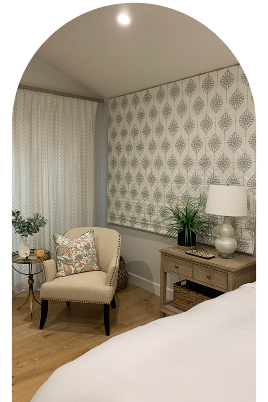 A bedroom with a chair , nightstand , table and lamp.