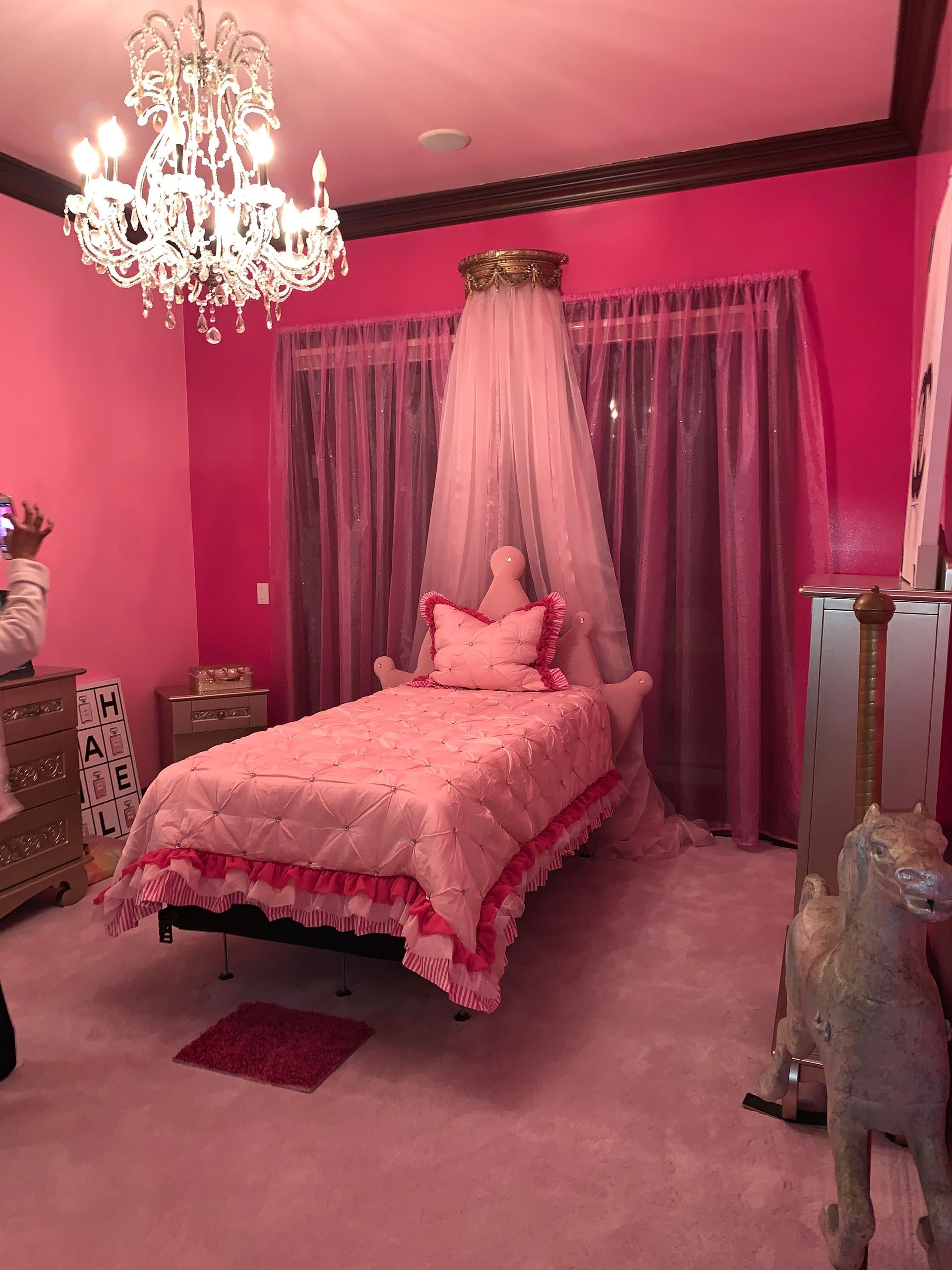 A bedroom with pink walls , a bed , a chandelier and a canopy.