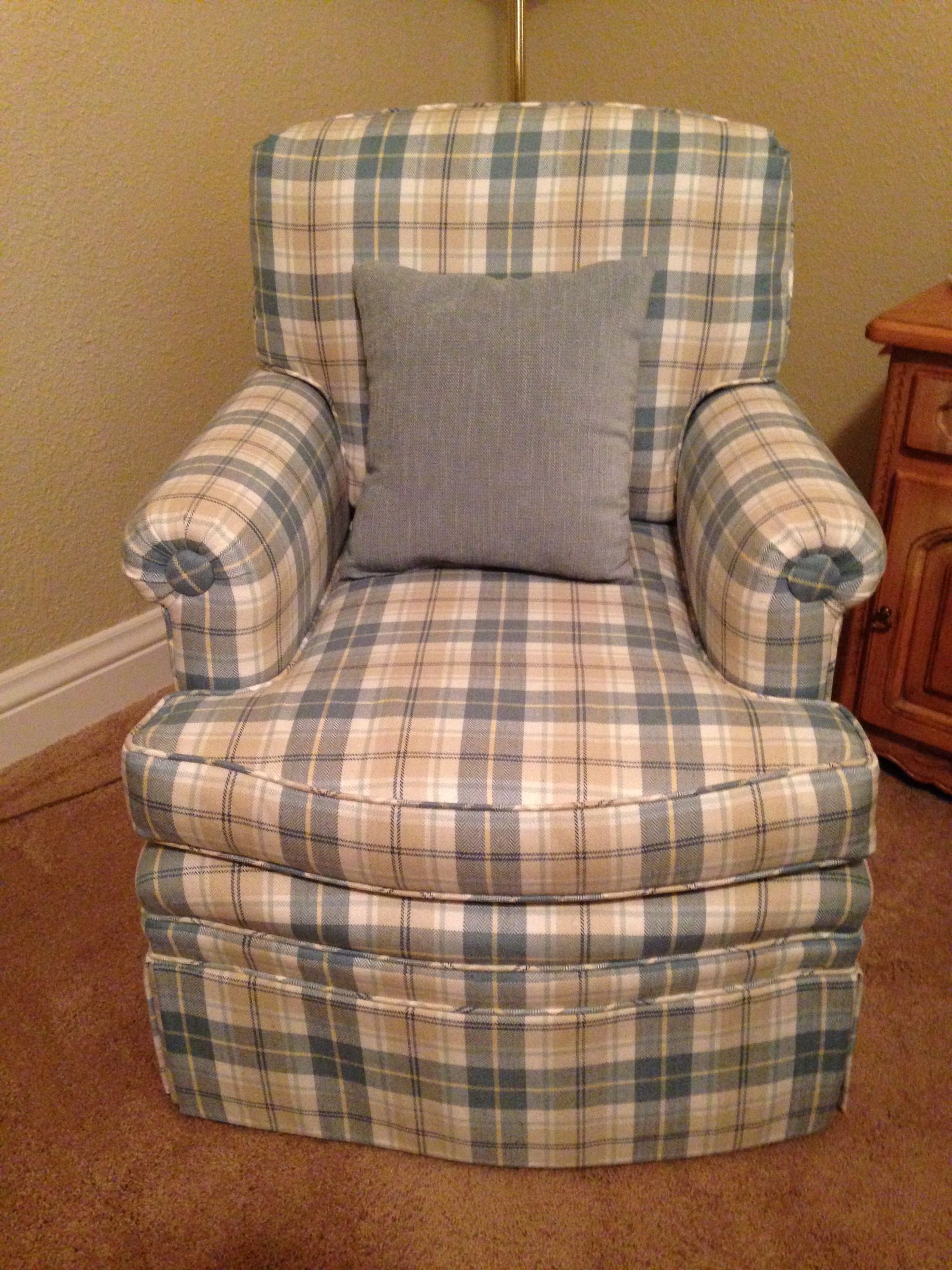 A plaid chair with a pillow on it is sitting in a room.