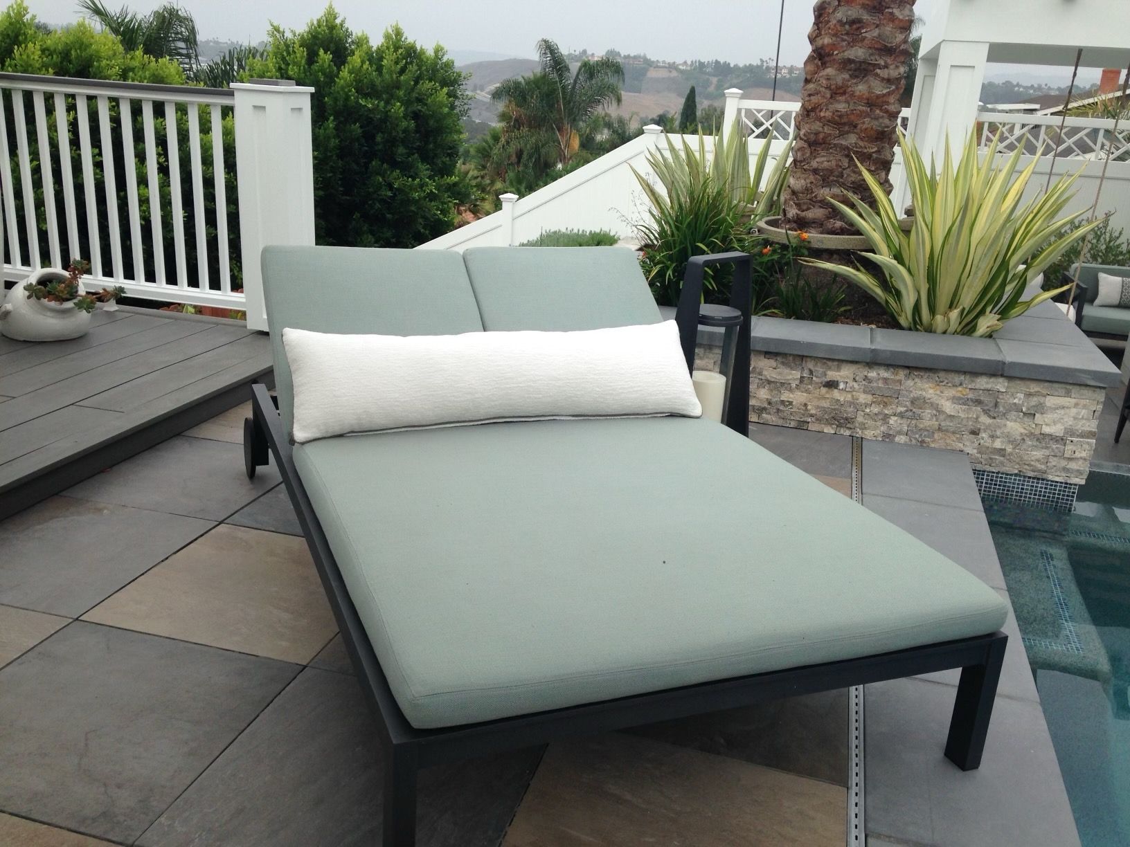 A lounge chair with a white pillow on it sits next to a pool