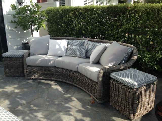 A curved wicker couch sits on a stone patio
