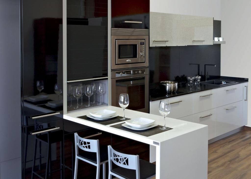 Cocina moderna con gabinetes en blanco y negro, microondas/horno empotrado, barra de desayuno con dos sillas y vajilla.