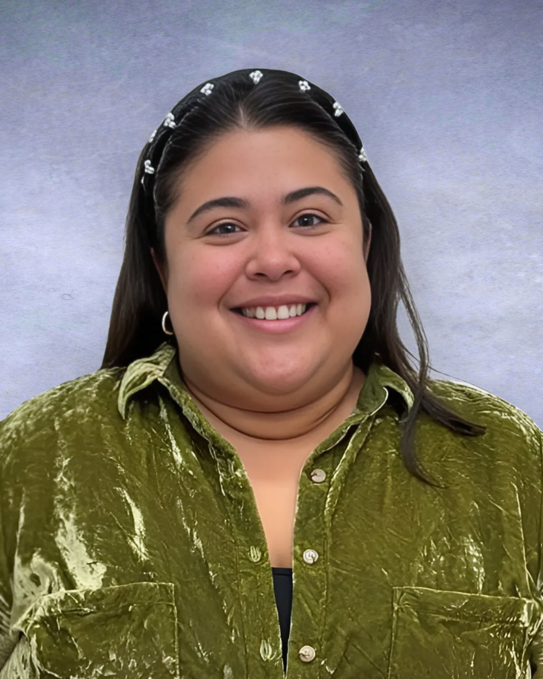 A person with dark hair and a pearl-studded headband smiling, wearing a textured, olive-green collared shirt.