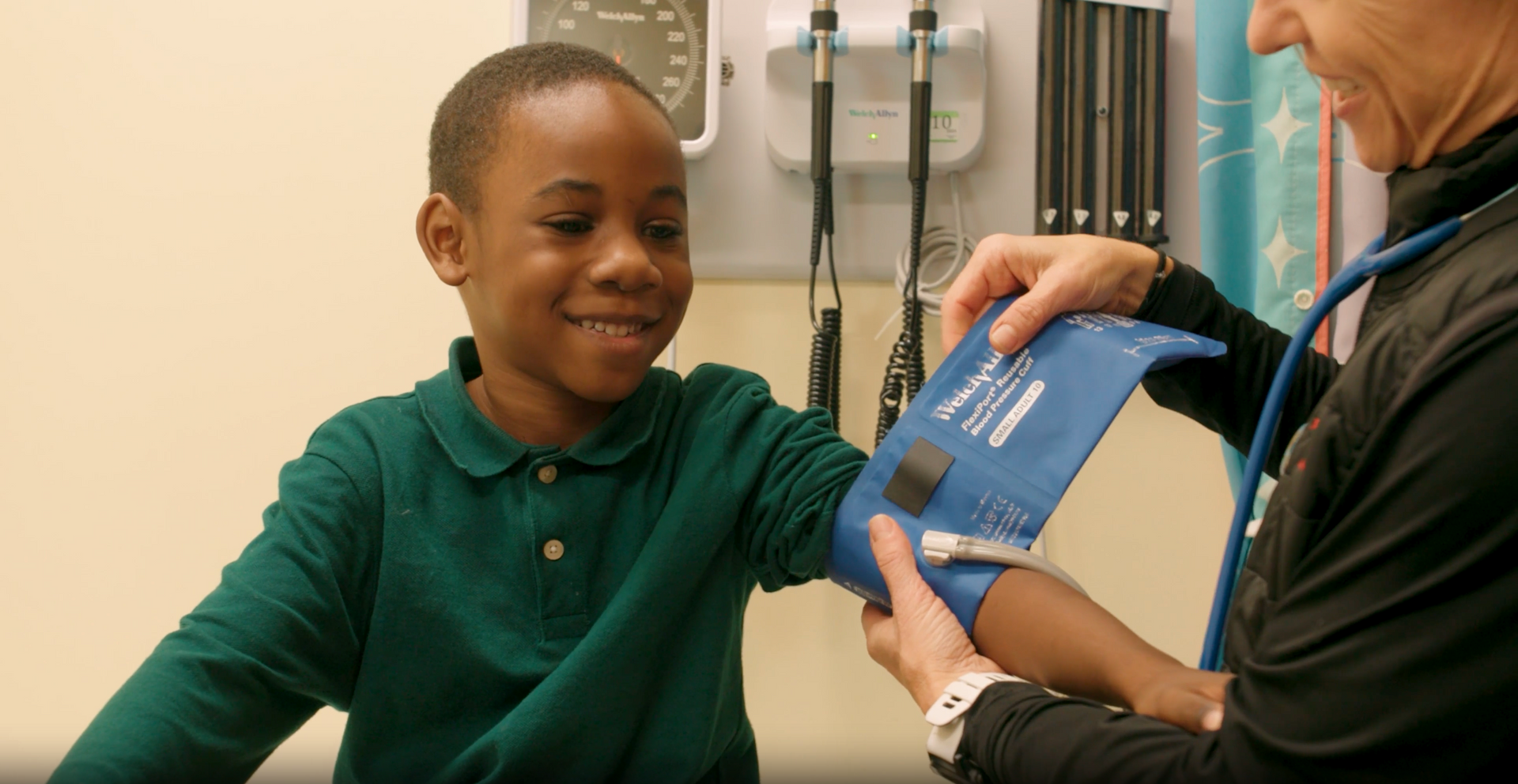 A healthcare professional wraps a blood pressure cuff around a patient's upper arm in an examination room.