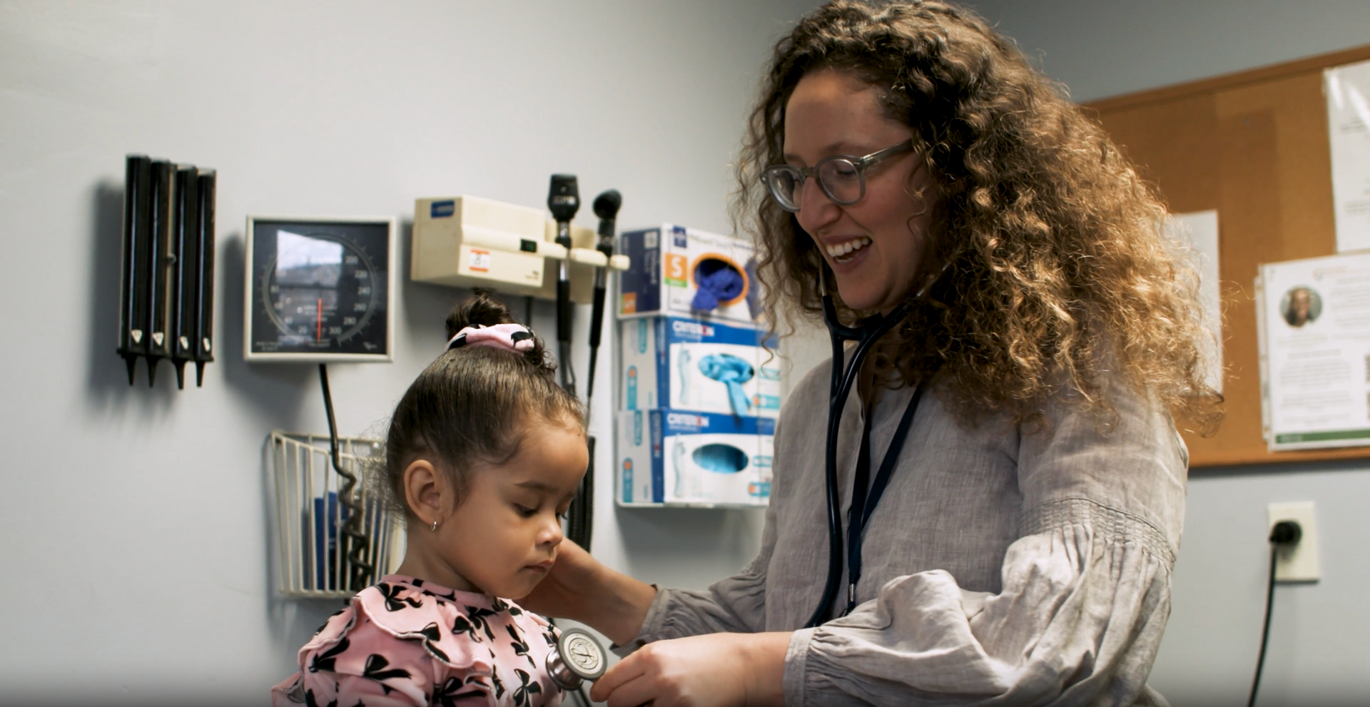 A healthcare professional uses a stethoscope to examine a young child in a medical office.