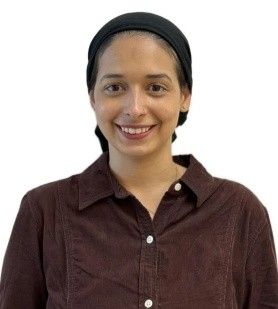 A person wearing a black headscarf and a brown button-up shirt smiling against a plain white background.
