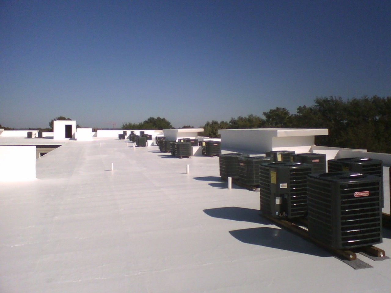 A row of black air conditioners on a white roof