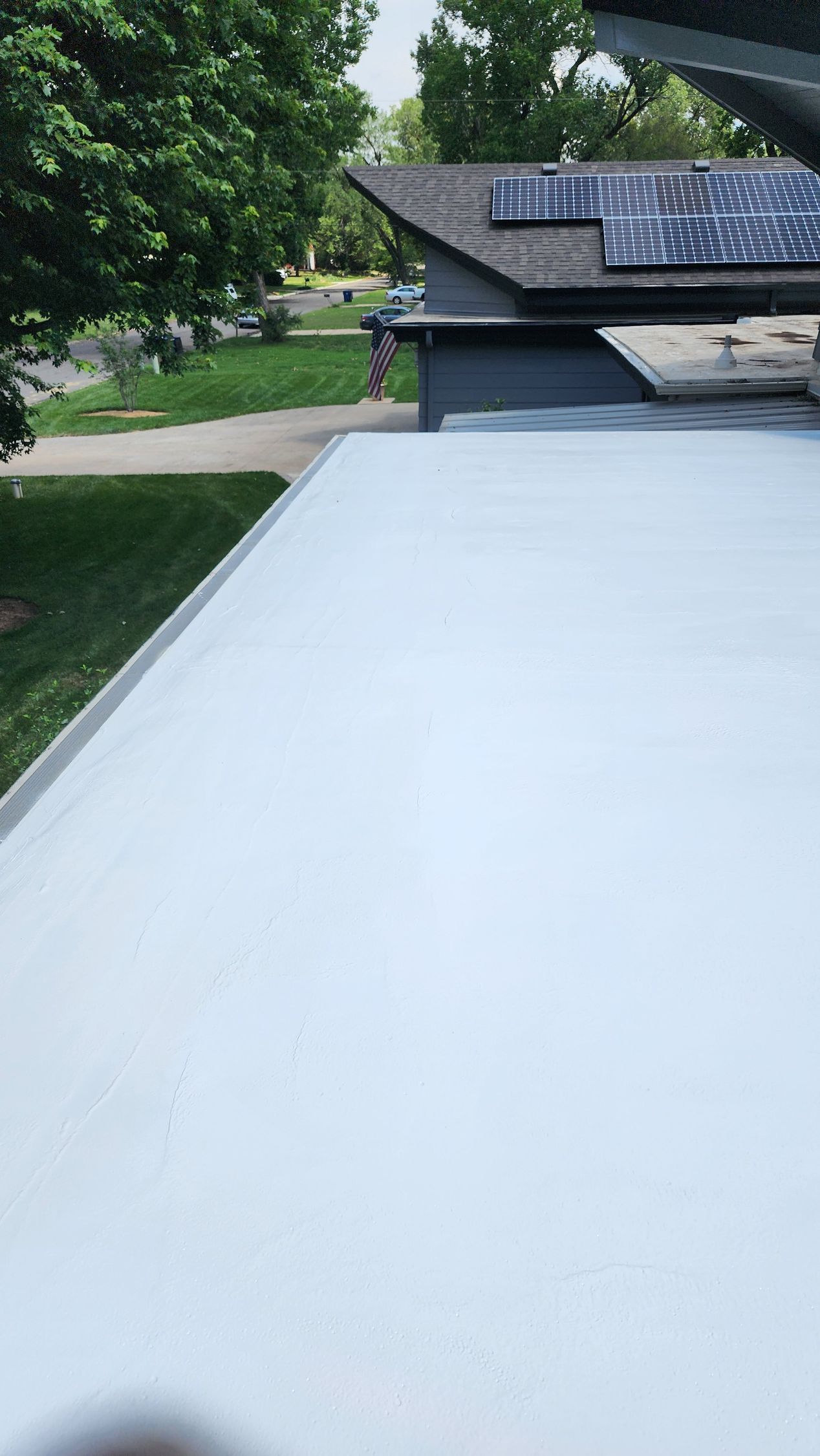 A white roof with solar panels on it and a house in the background.