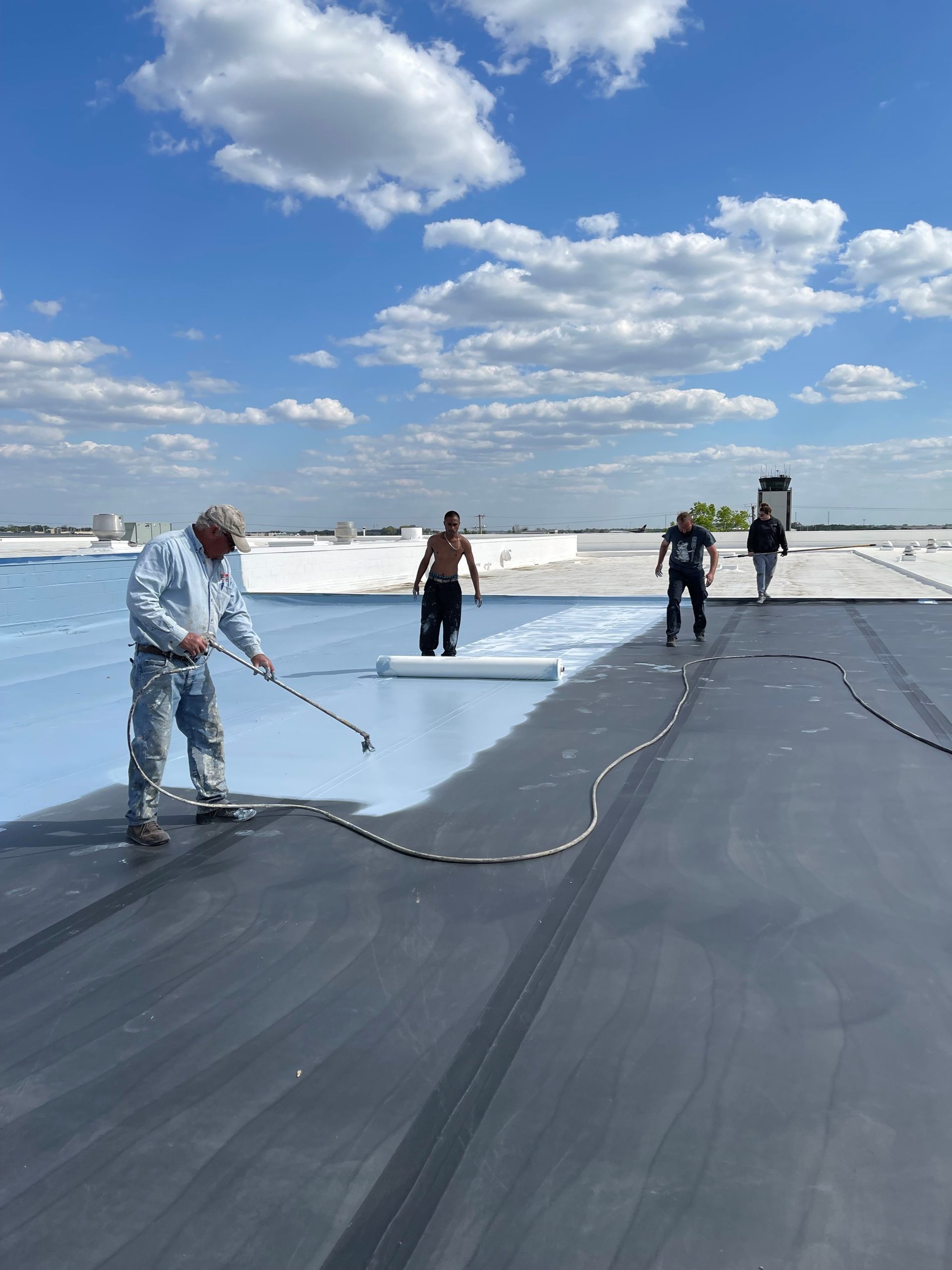 A group of men are painting a roof with a roller.