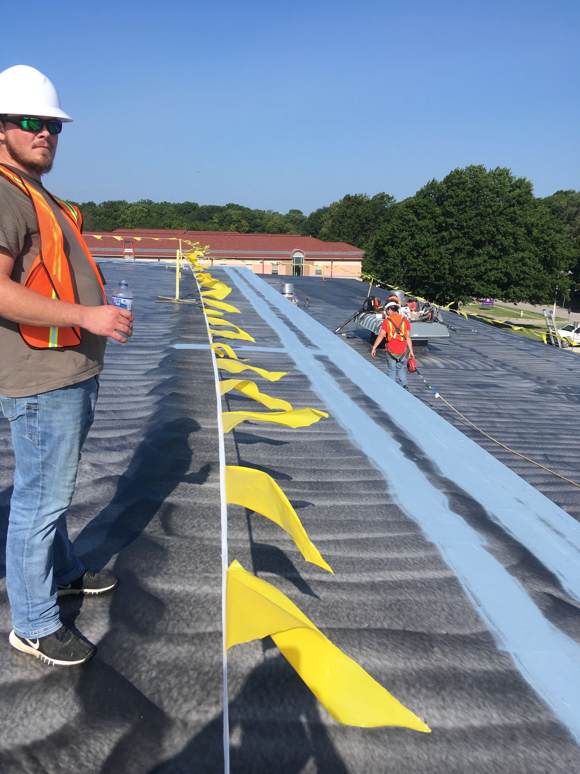 A man in a hard hat stands on a roof with yellow flags