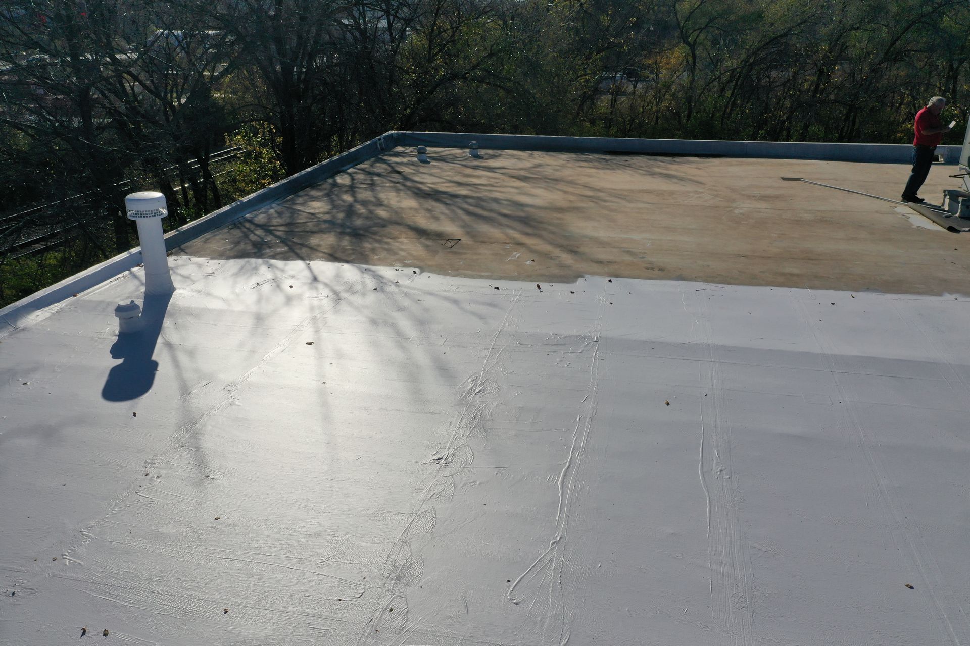 A man is standing on top of a roof with trees in the background.