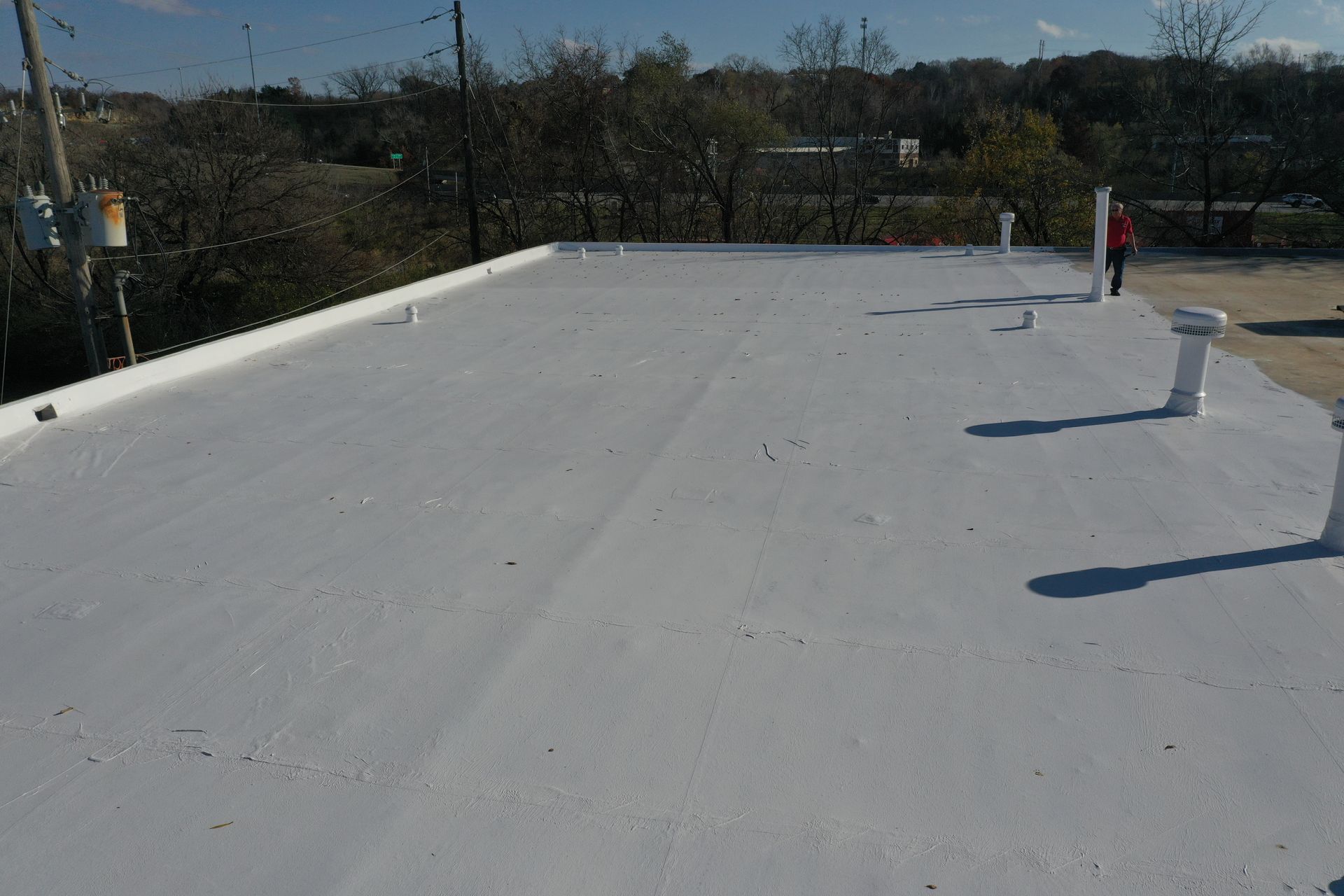 A person is standing on a white roof with trees in the background.