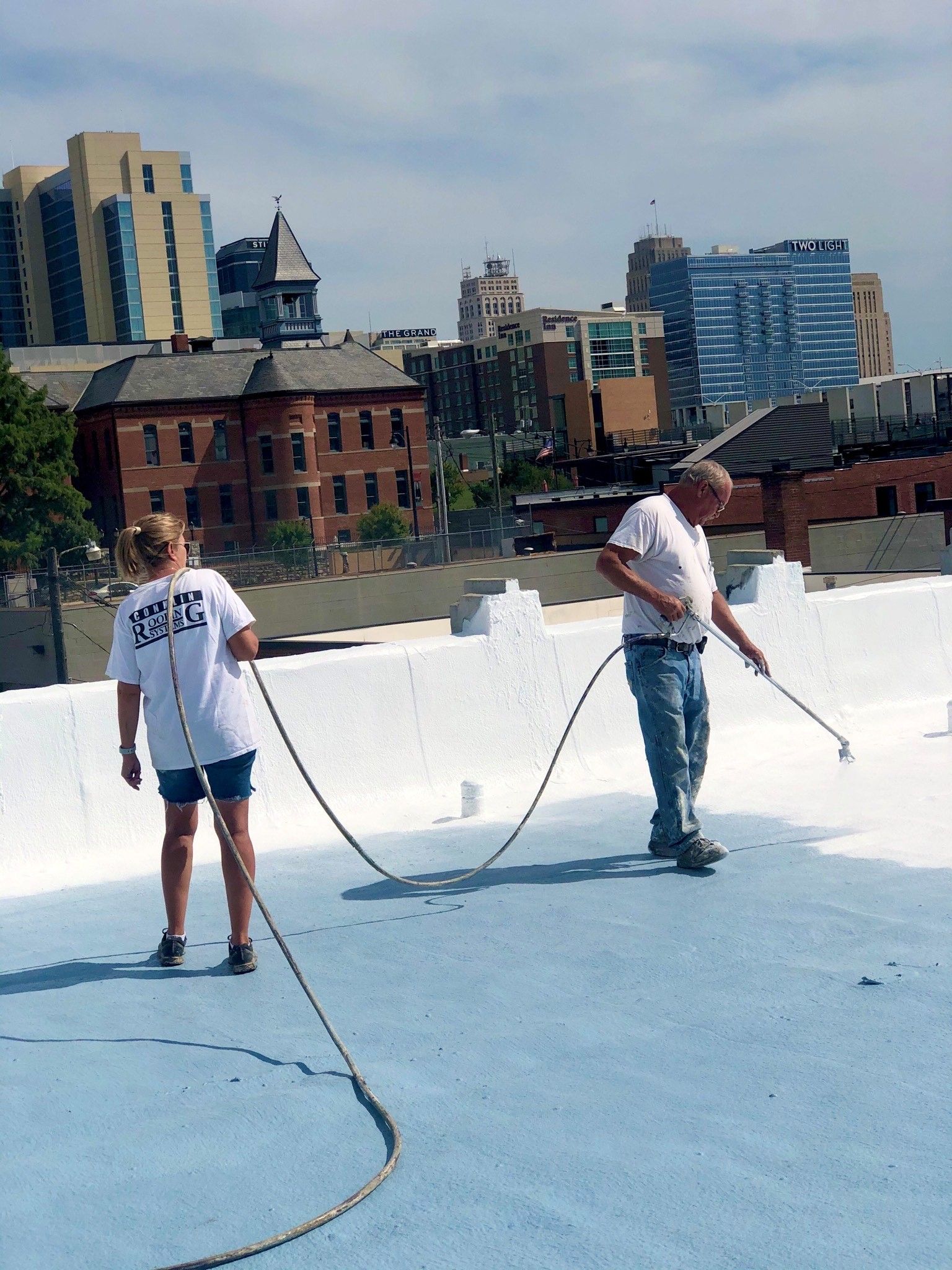 A man and a woman are painting a roof with a city in the background