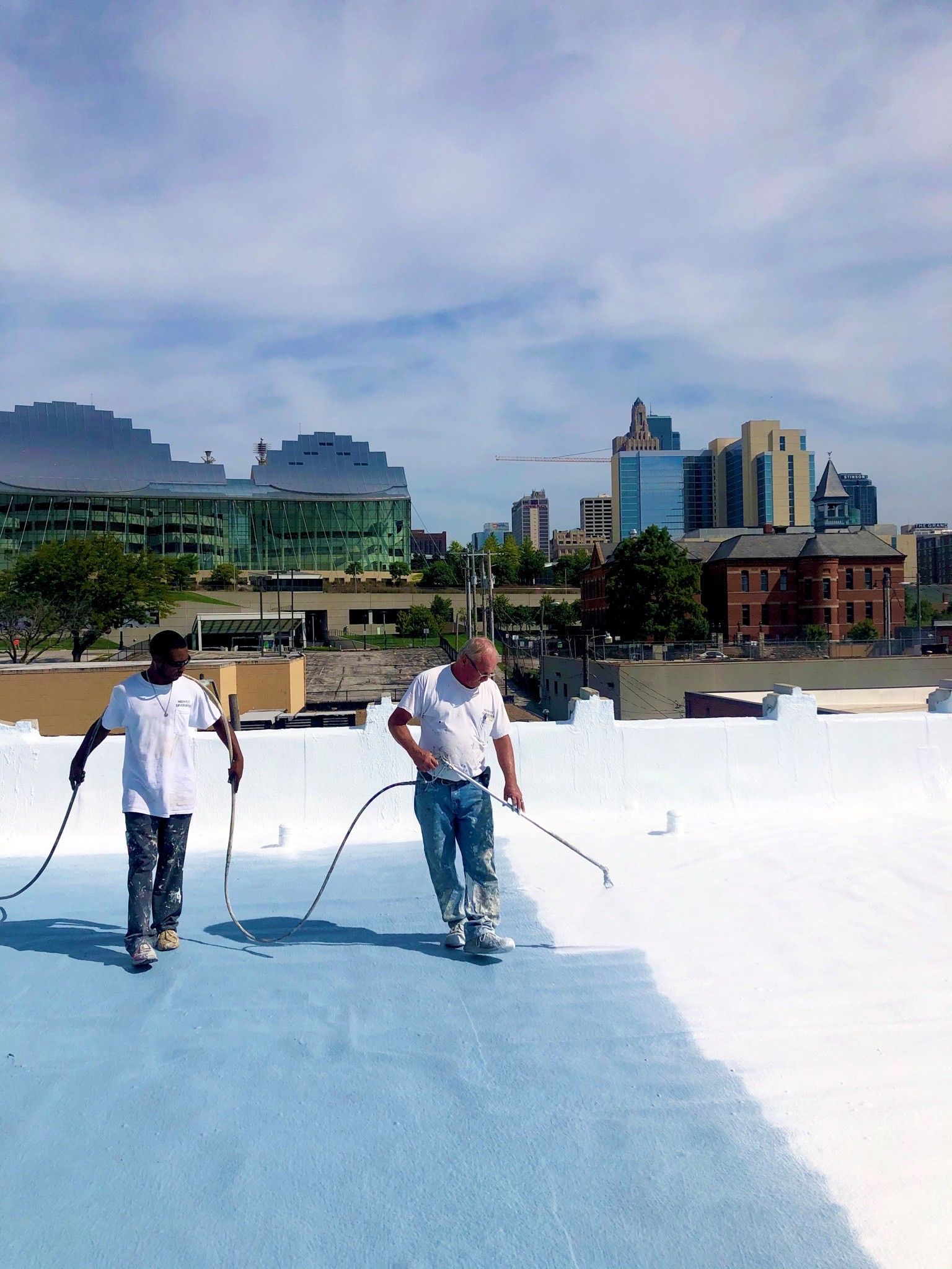Two men are painting a roof with a city in the background
