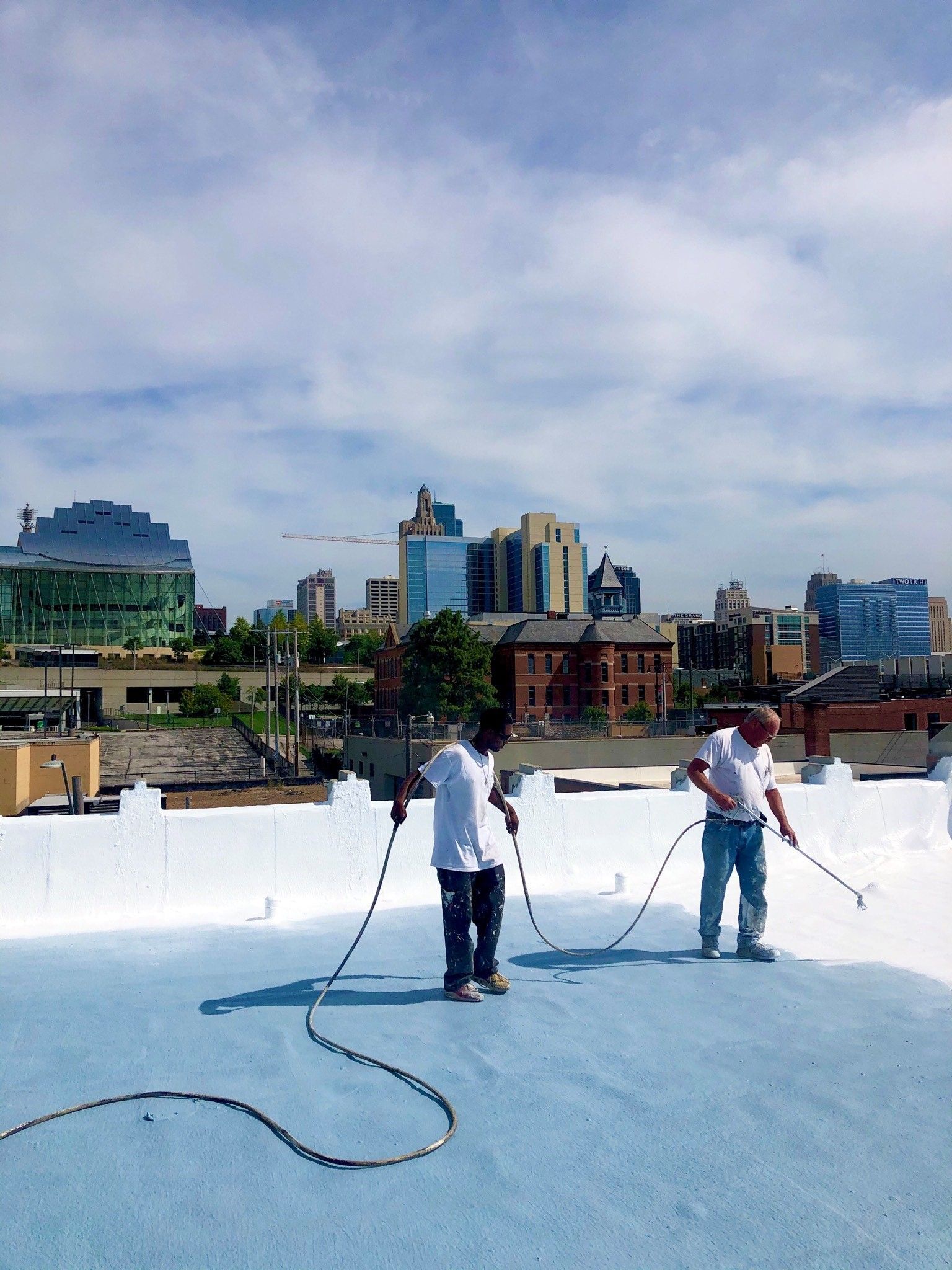 Two men are working on a roof with a city in the background