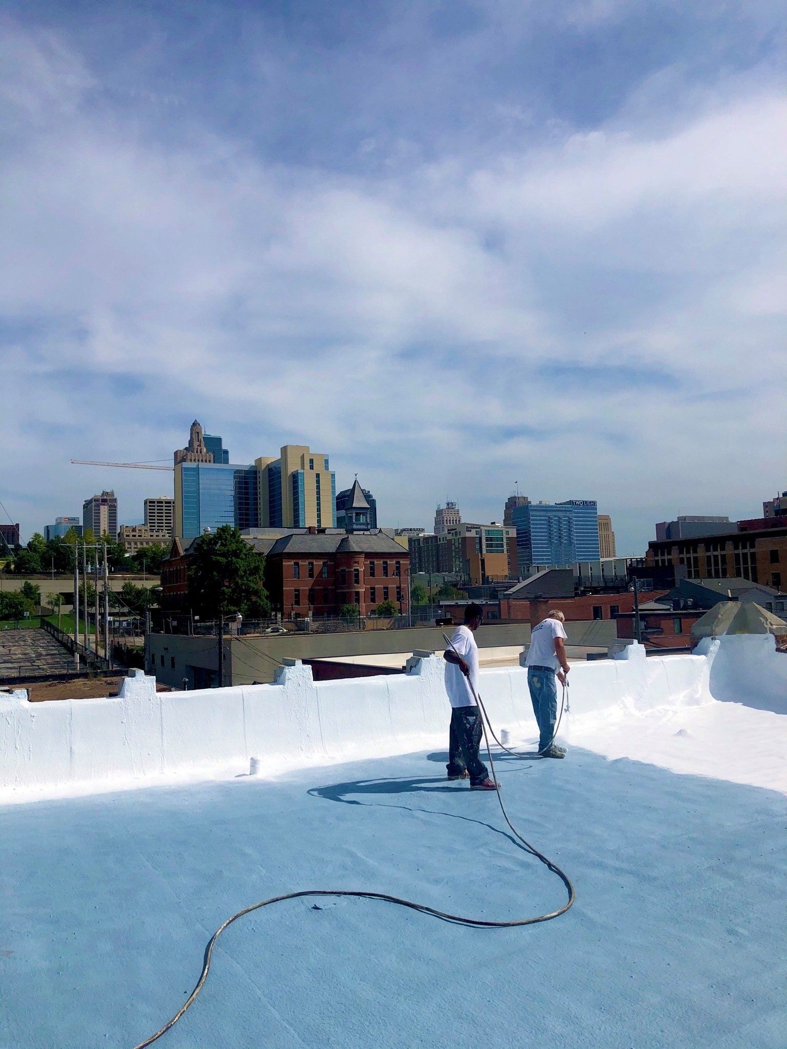 Two men are working on a roof with a city in the background