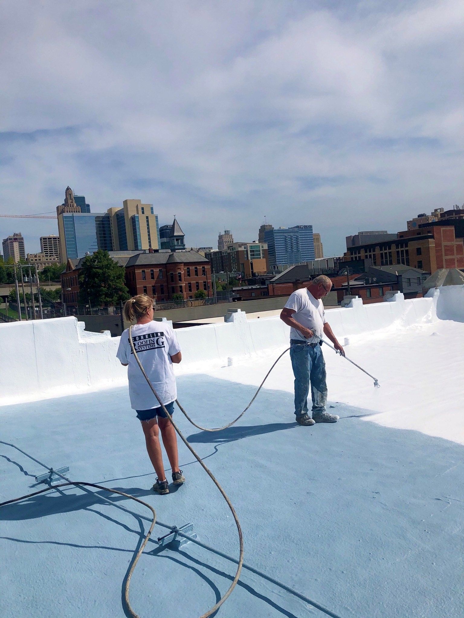 A man and a woman are spraying paint on a roof.