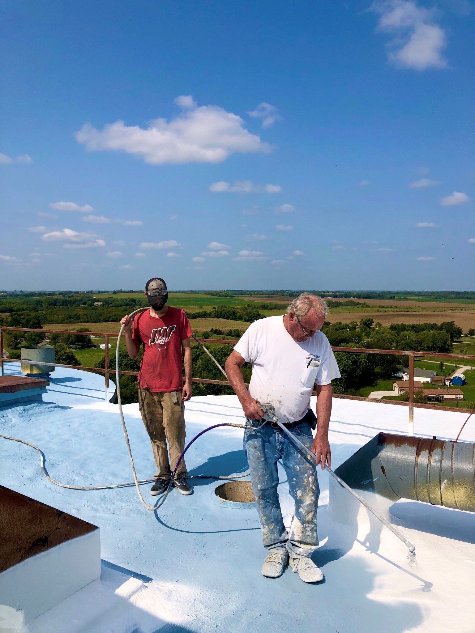 Two men are standing on top of a roof painting it.