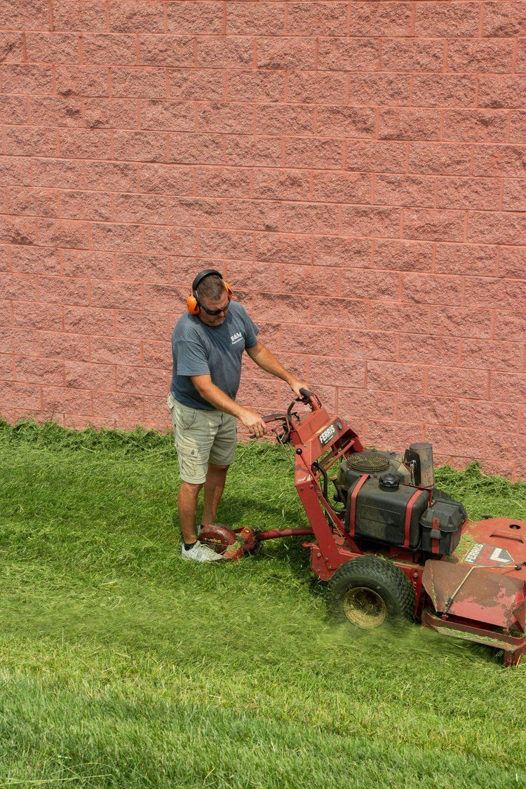 A man is standing next to a lawn mower cutting grass.