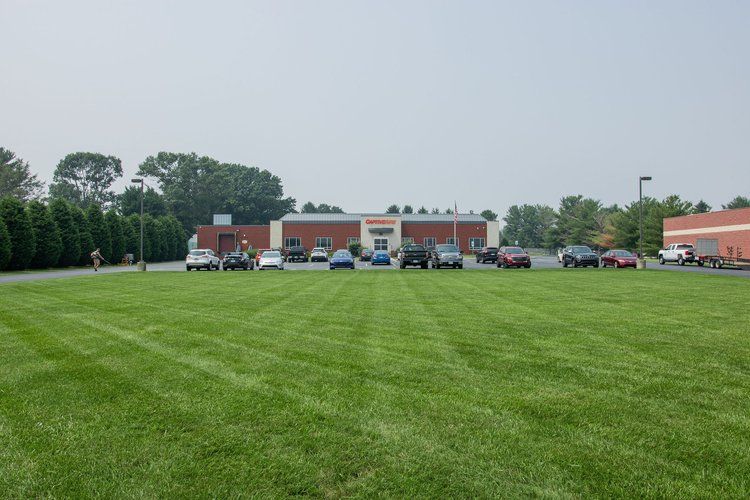 A row of cars are parked in a grassy field in front of a building