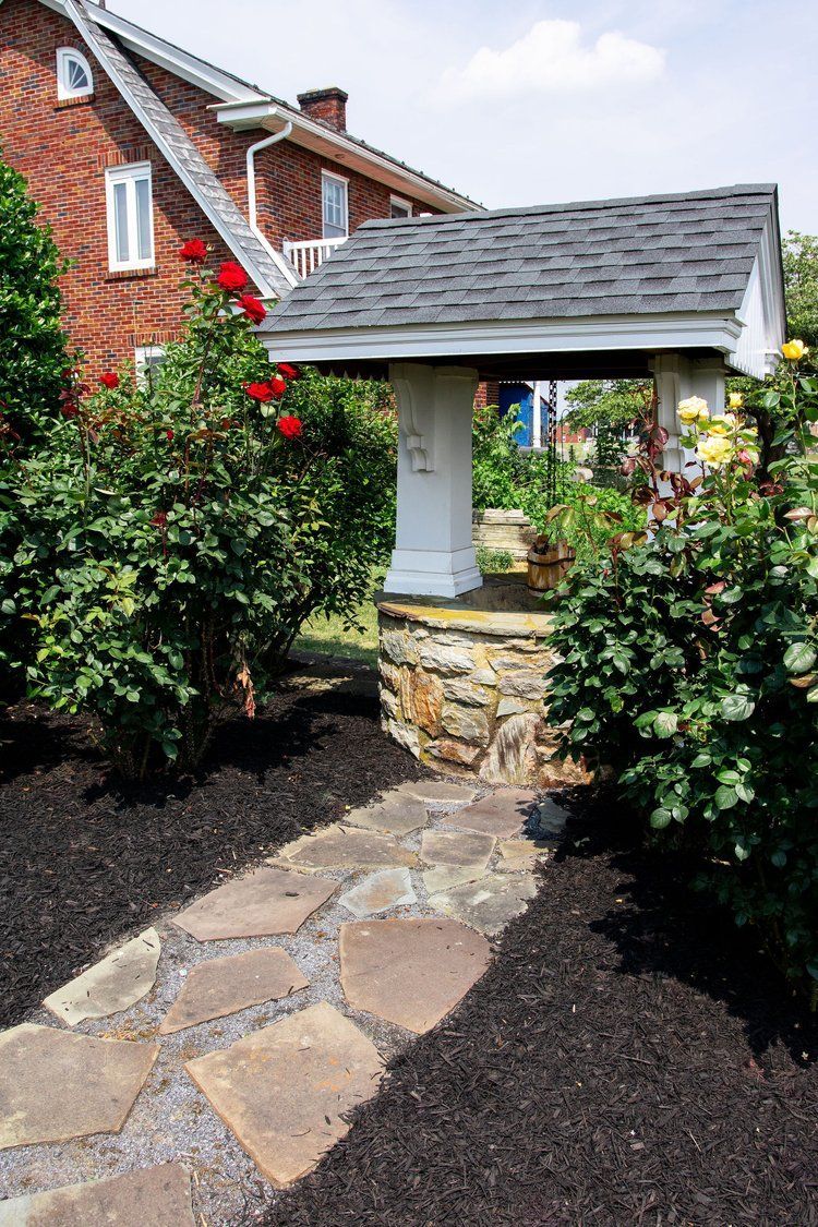 A stone walkway leading to a well in front of a brick house.