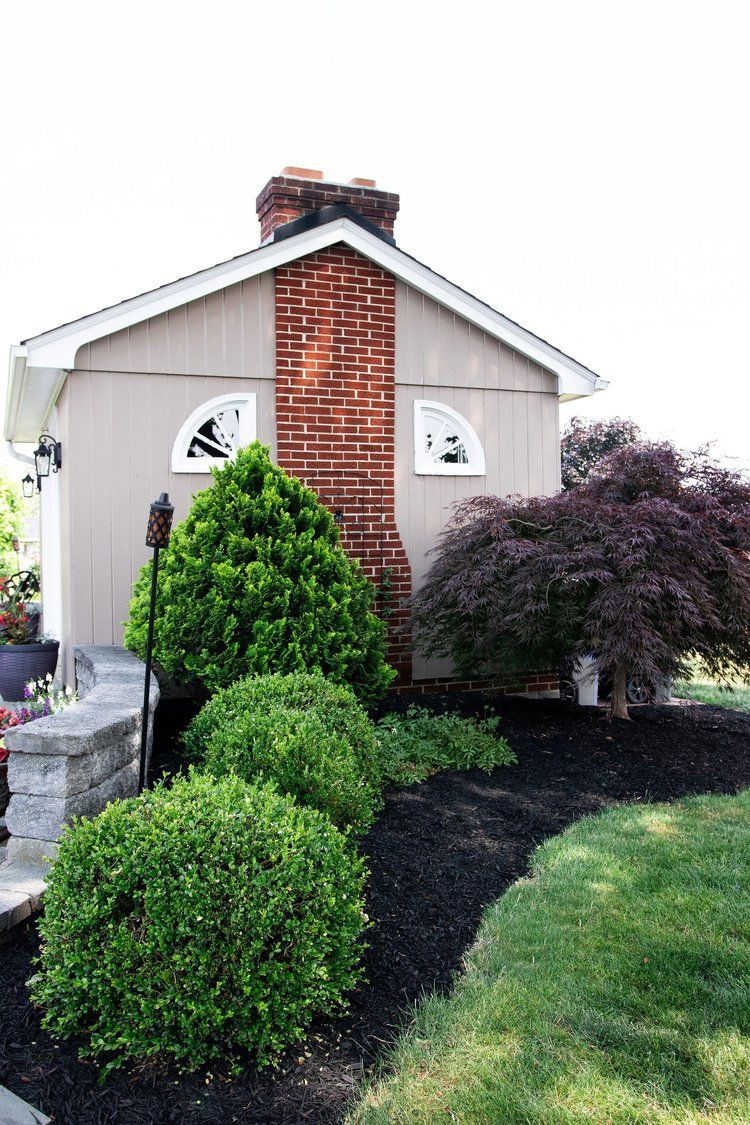 A small house with a brick chimney is surrounded by bushes and trees.