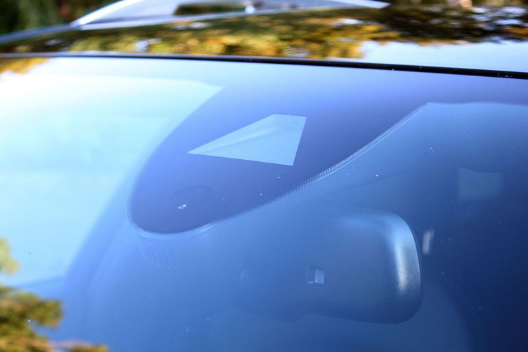 Windshield of a black car with a sensor and rearview mirror visible.
