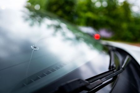 Close-up of a windshield with a crack. Blurred green trees and a red light in the background.