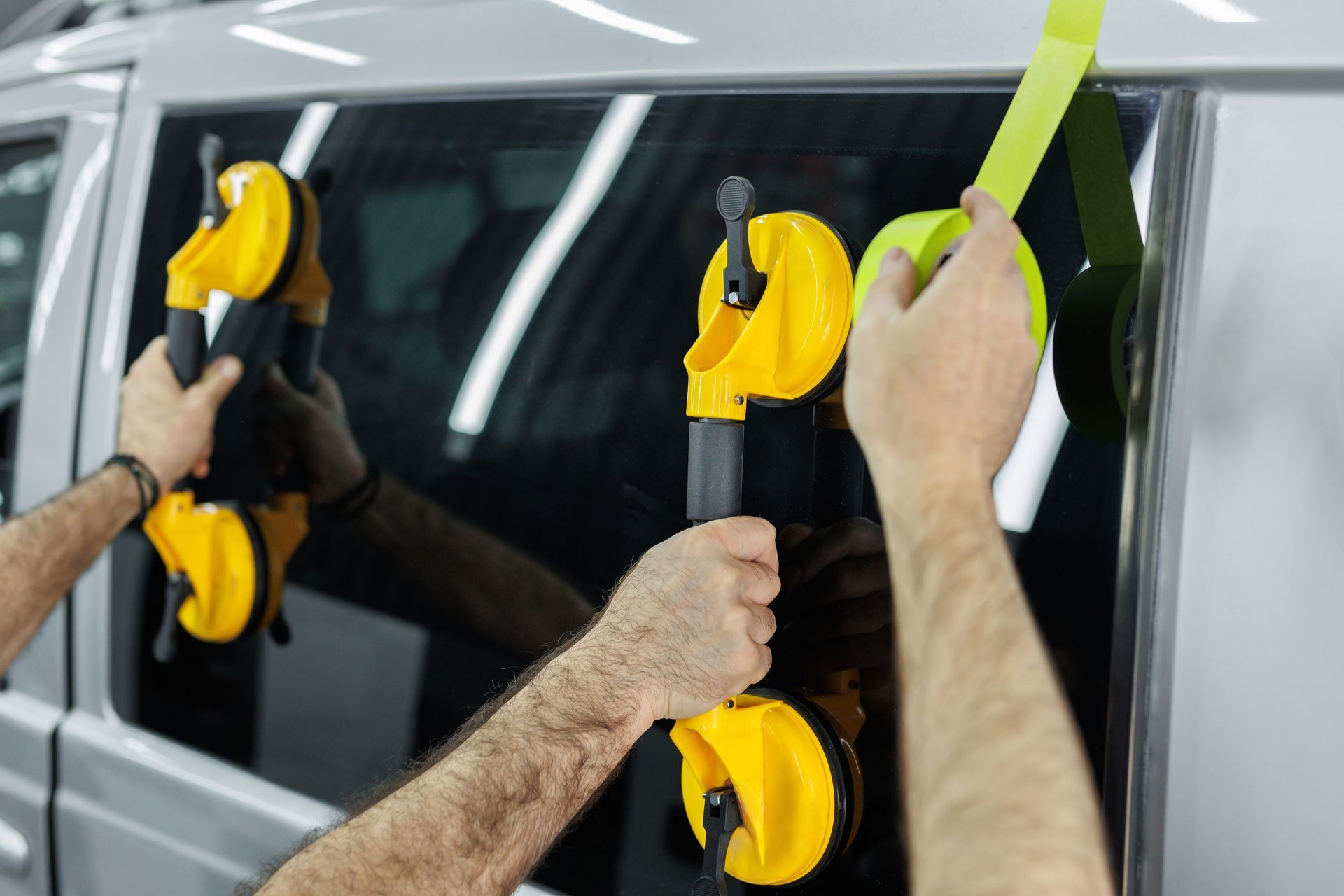 Hands using yellow suction cups to remove a vehicle window.