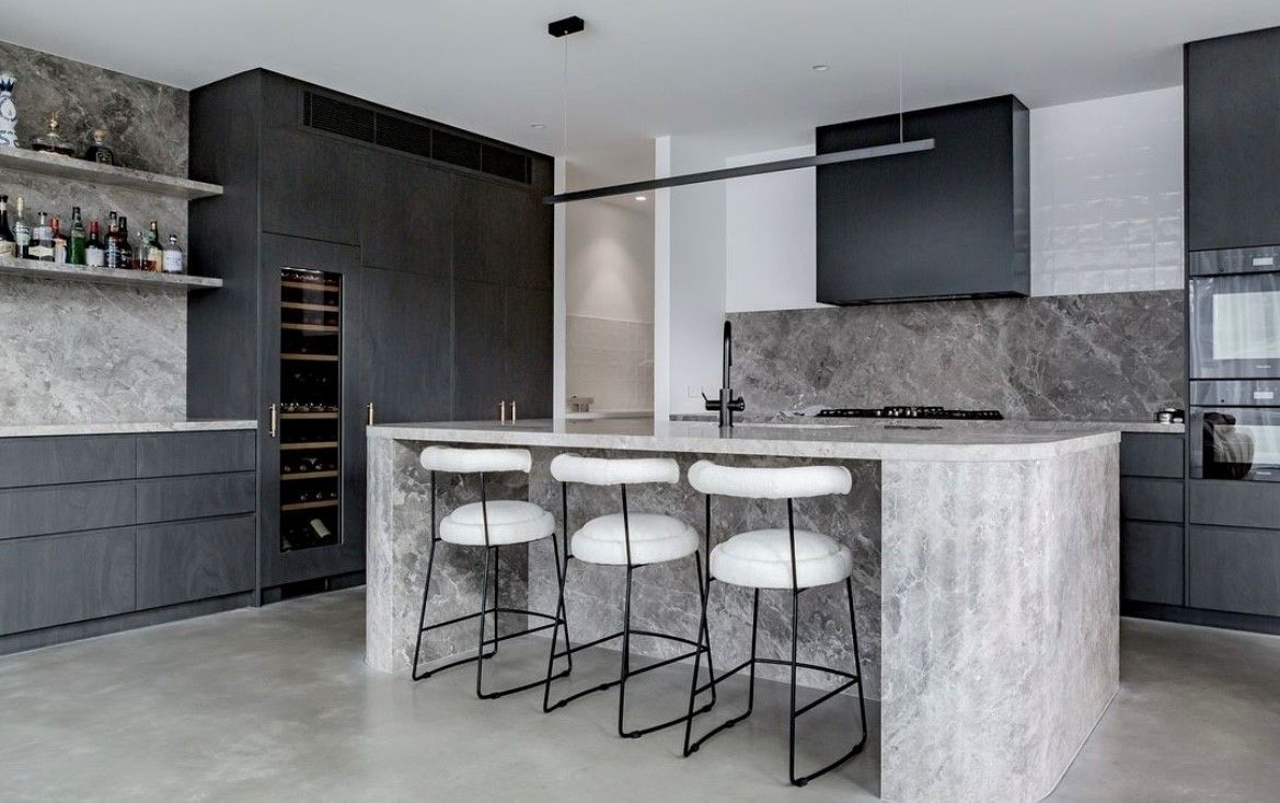 Modern kitchen with grey cabinetry, island with white stools, and marble backsplash — Inovative Interiors In Cardiff, NSW