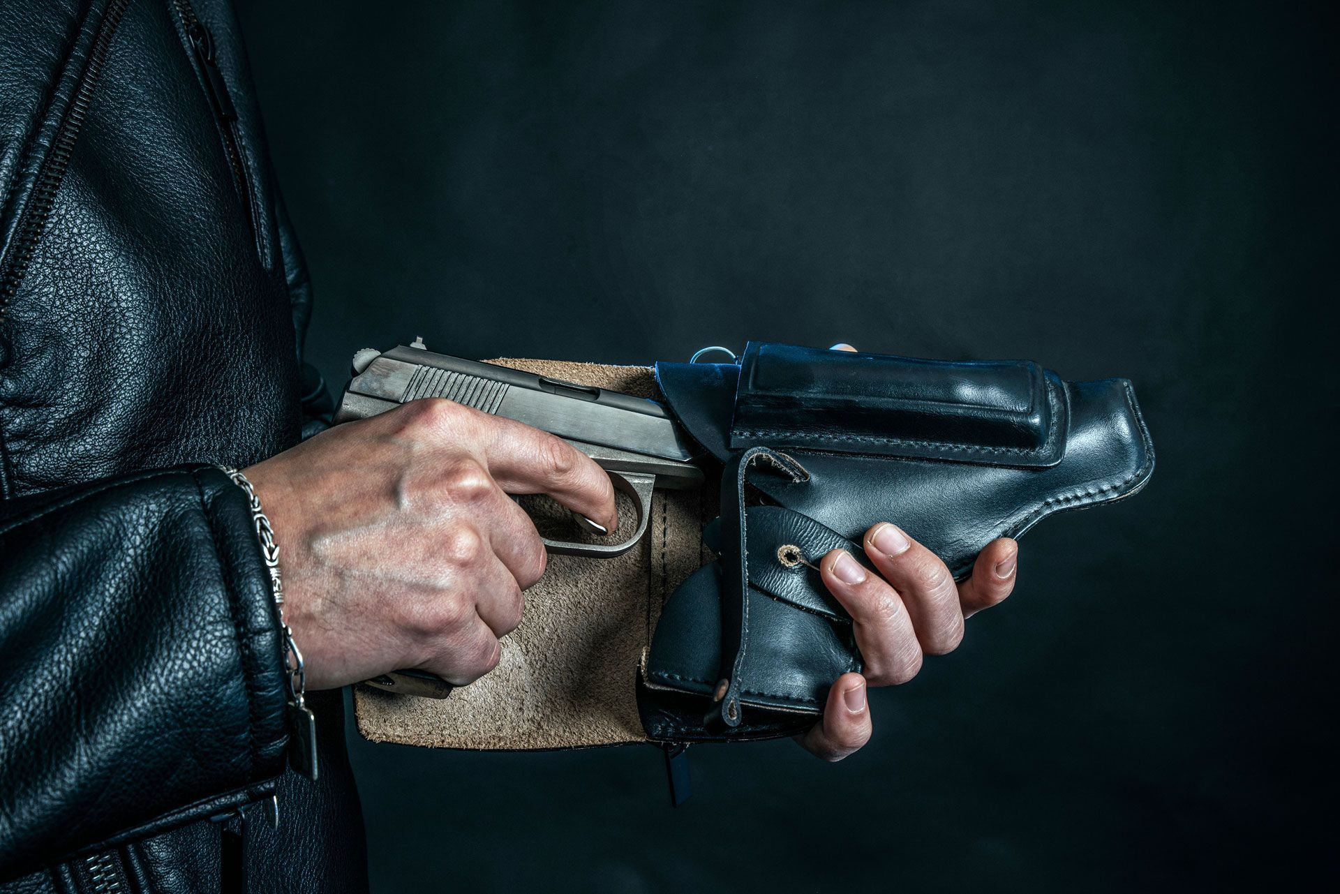 Person holding a handgun in a black leather holster, set against a dark background.