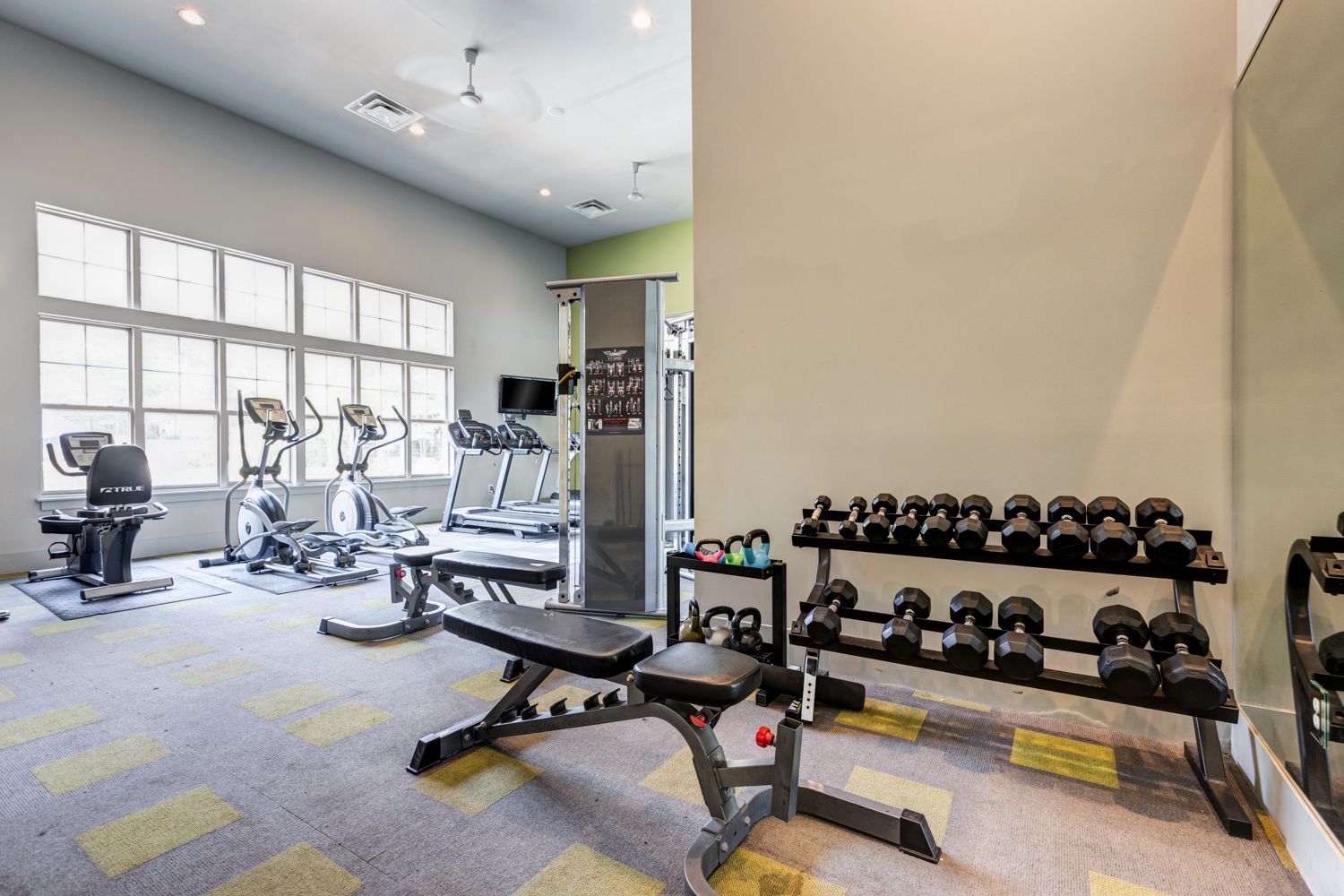 Gym with exercise equipment: treadmills, weights, and bench. Bright room with large windows at Arcadia's Edge in Columbia, SC.